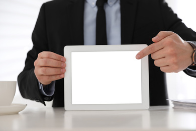 Businessman holding modern tablet with blank screen at white table in office, closeup