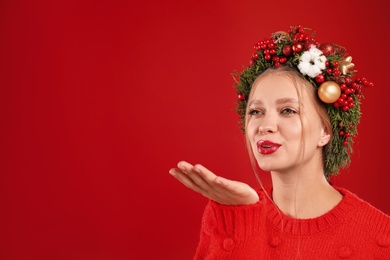 Beautiful young woman wearing Christmas wreath on red background. Space for text