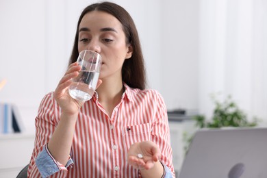 Photo of Young woman taking pill against headache in office