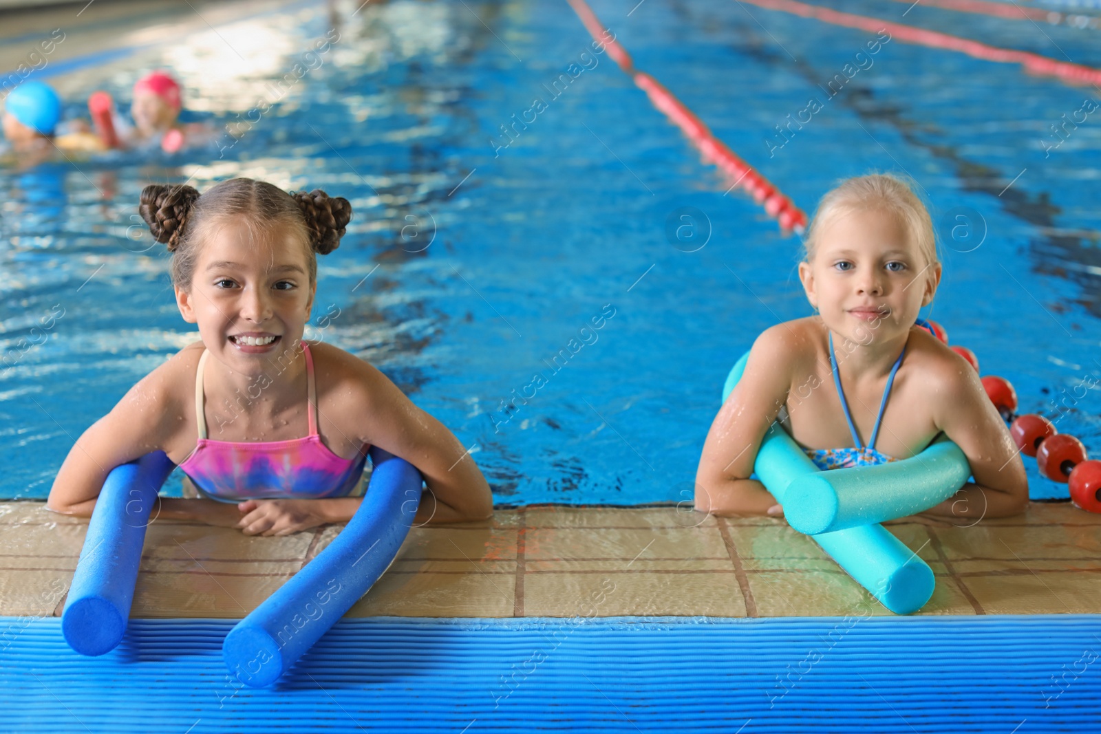 Photo of Little girls with swimming noodles in indoor pool