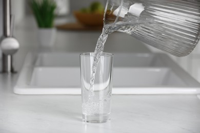 Photo of Pouring water from jug into glass on white countertop in kitchen