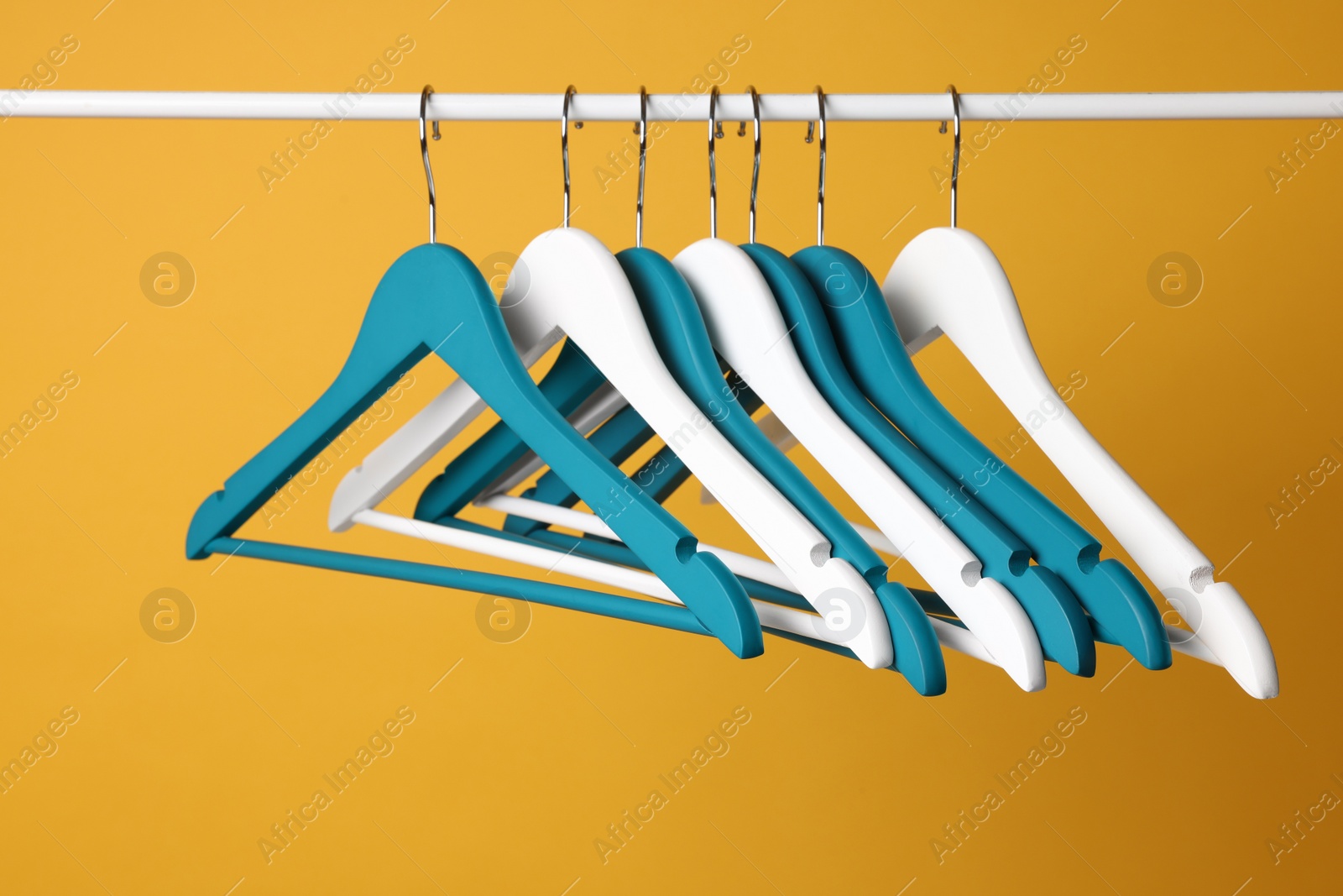 Photo of Empty clothes hangers on metal rail against yellow background