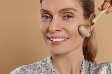 Photo of Woman massaging her face with jade roller on beige background