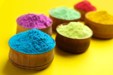 Photo of Colorful powders in wooden bowls on yellow background. Holi festival celebration