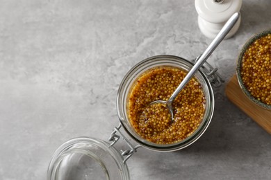 Bowl and jar of delicious whole grain mustard on grey table, flat lay. Space for text