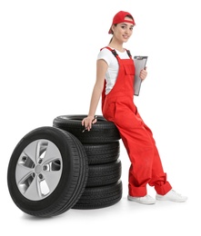 Female mechanic in uniform with car tires and clipboard on white background