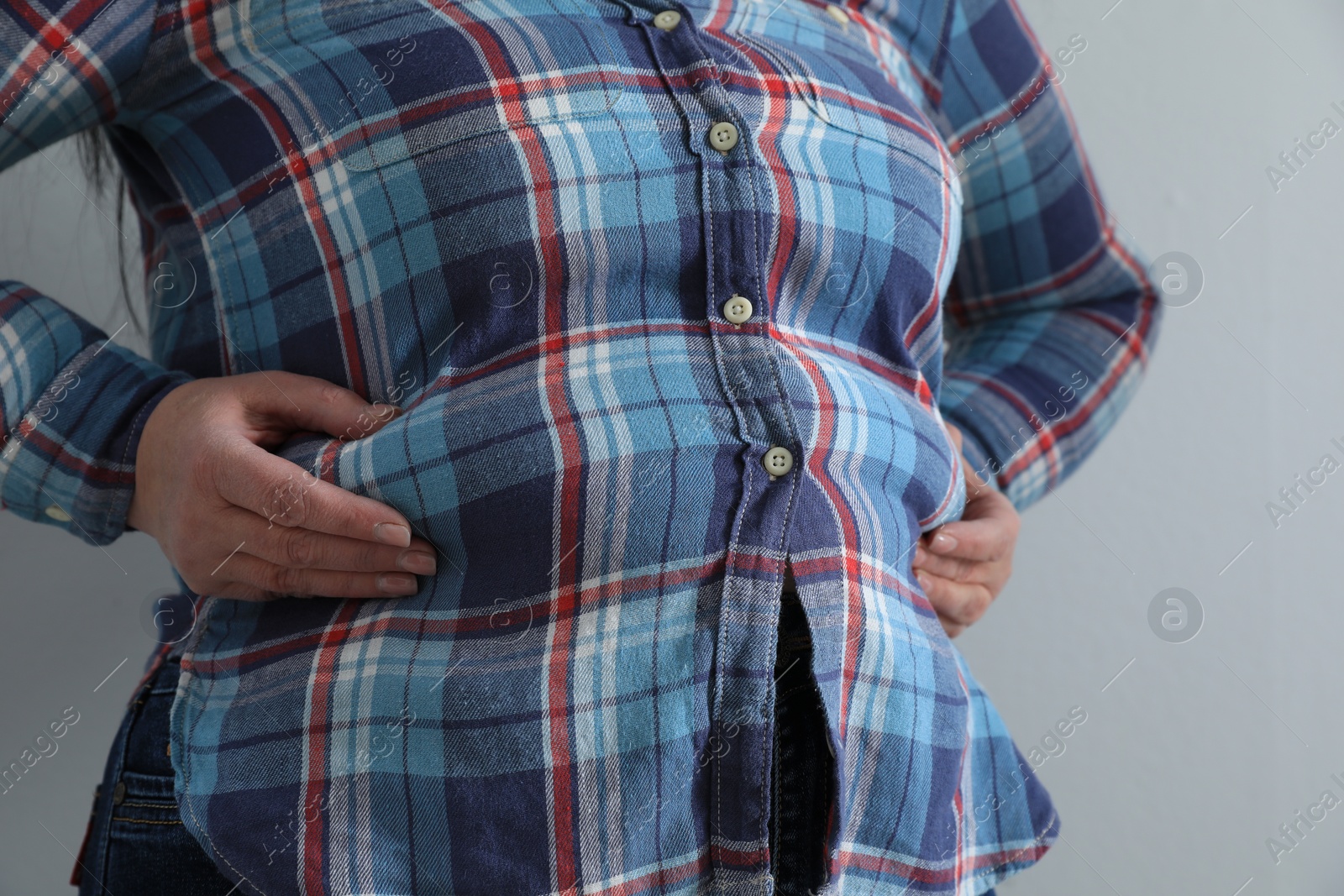 Photo of Overweight woman in tight shirt on light grey background, closeup