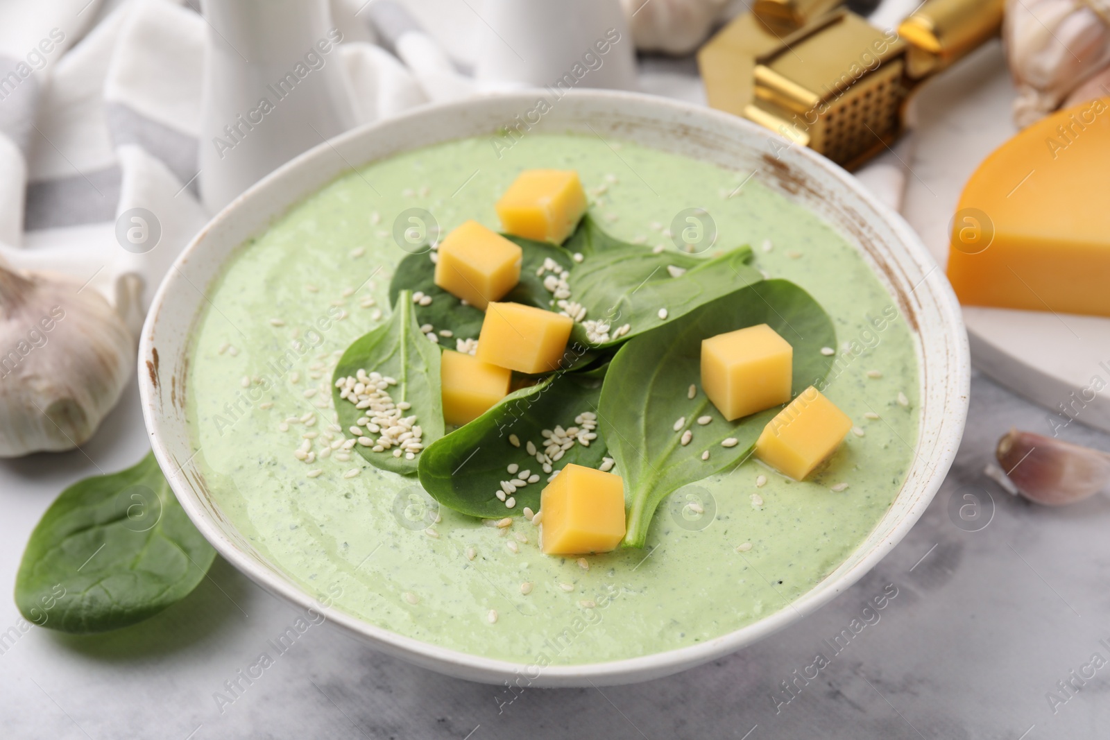 Photo of Delicious spinach cream soup with cheese and sesame seeds in bowl on white marble table