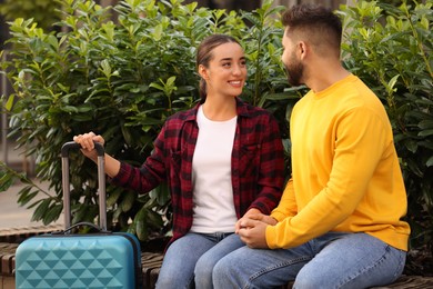 Long-distance relationship. Beautiful happy couple on bench and suitcase outdoors