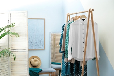 Photo of Wardrobe rack with women's clothes at color wall in room