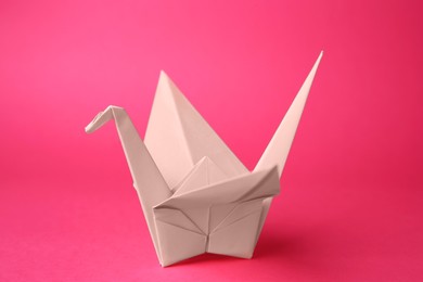 Photo of Origami art. Handmade paper crane on pink background, closeup