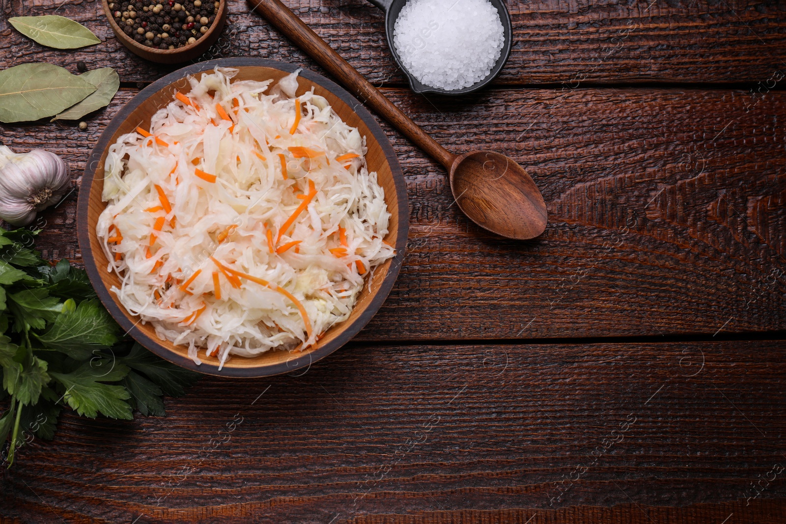 Photo of Bowl of tasty sauerkraut and ingredients on wooden table, flat lay. Space for text