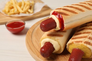 Photo of Delicious french hot dogs, fries and dip sauce on white wooden table, closeup
