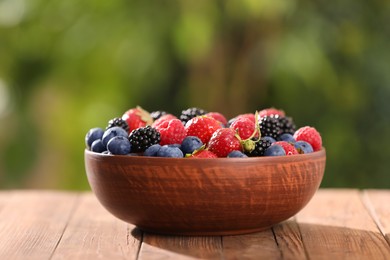 Bowl with different fresh ripe berries on wooden table outdoors