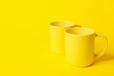 Photo of Two ceramic mugs on yellow background, space for text