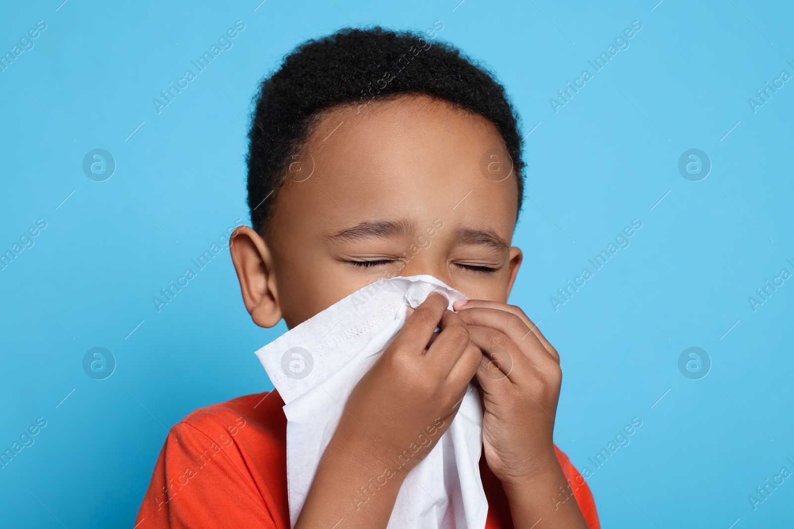 Photo of African-American boy blowing nose in tissue on turquoise background. Cold symptoms