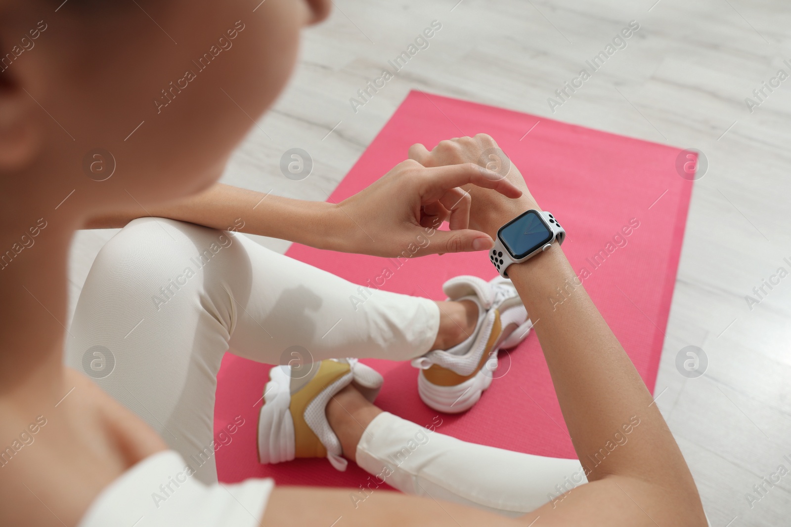 Photo of Young woman using smart watch during training indoors, closeup