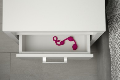 Photo of Pink anal balls in open drawer of bedside table indoors, above view. Sex toy