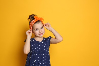 Photo of Cute little girl wearing stylish bandana on orange background, space for text