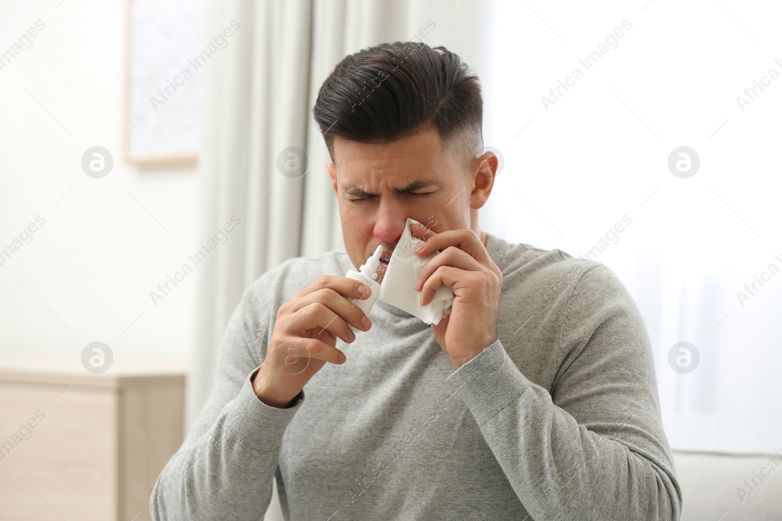 Photo of Ill man with paper tissue using nasal spray at home