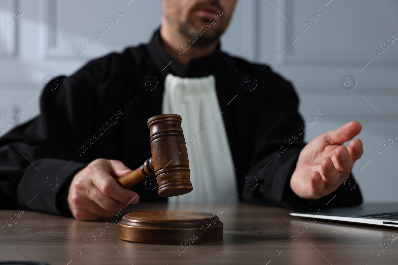 Photo of Judge with gavel and laptop sitting at wooden table indoors, closeup