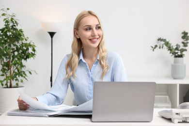 Happy secretary working with documents at table in office