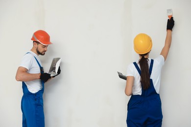 Photo of Professional workers plastering wall with putty knives in hard hats