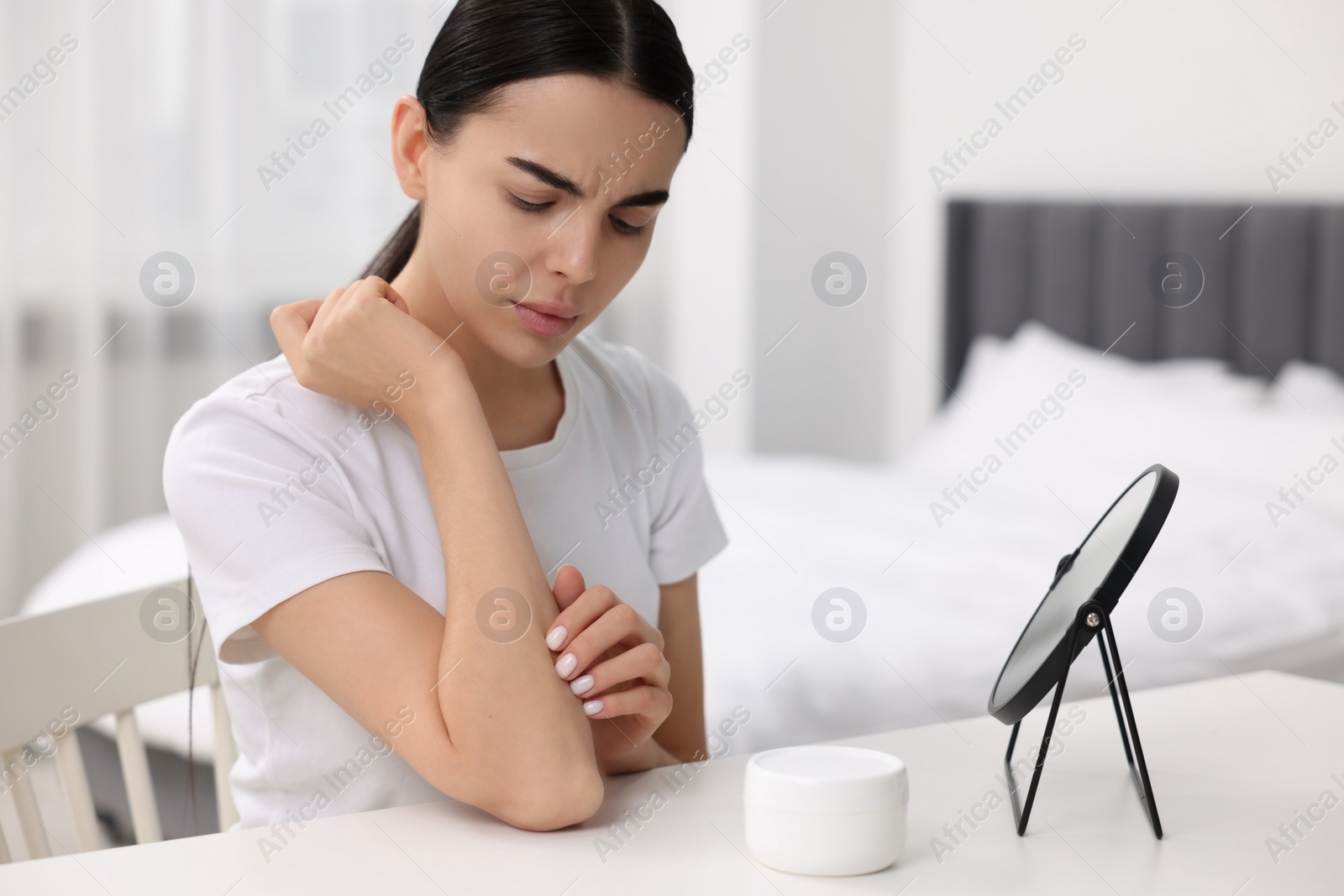 Photo of Woman with dry skin checking her arm at table indoors