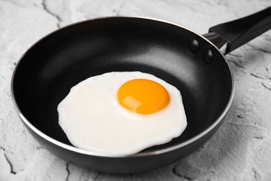 Tasty fried egg in pan on white textured table, closeup