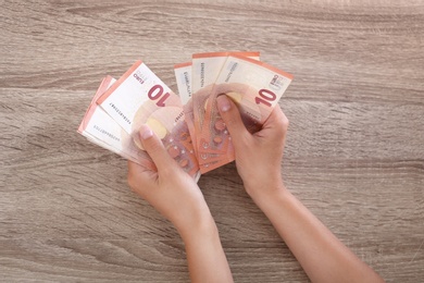 Woman with Euro banknotes at wooden table, top view