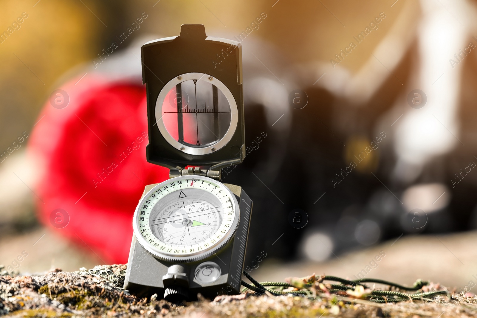 Photo of Compass on rock against blurred background, space for text. Camping equipment