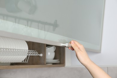 Photo of Woman opening cabinet with plates in kitchen, closeup