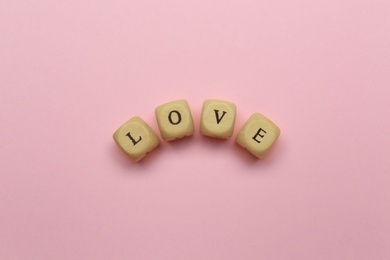 Mini cubes with letters forming word Love on pink background, flat lay