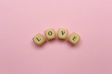 Photo of Mini cubes with letters forming word Love on pink background, flat lay