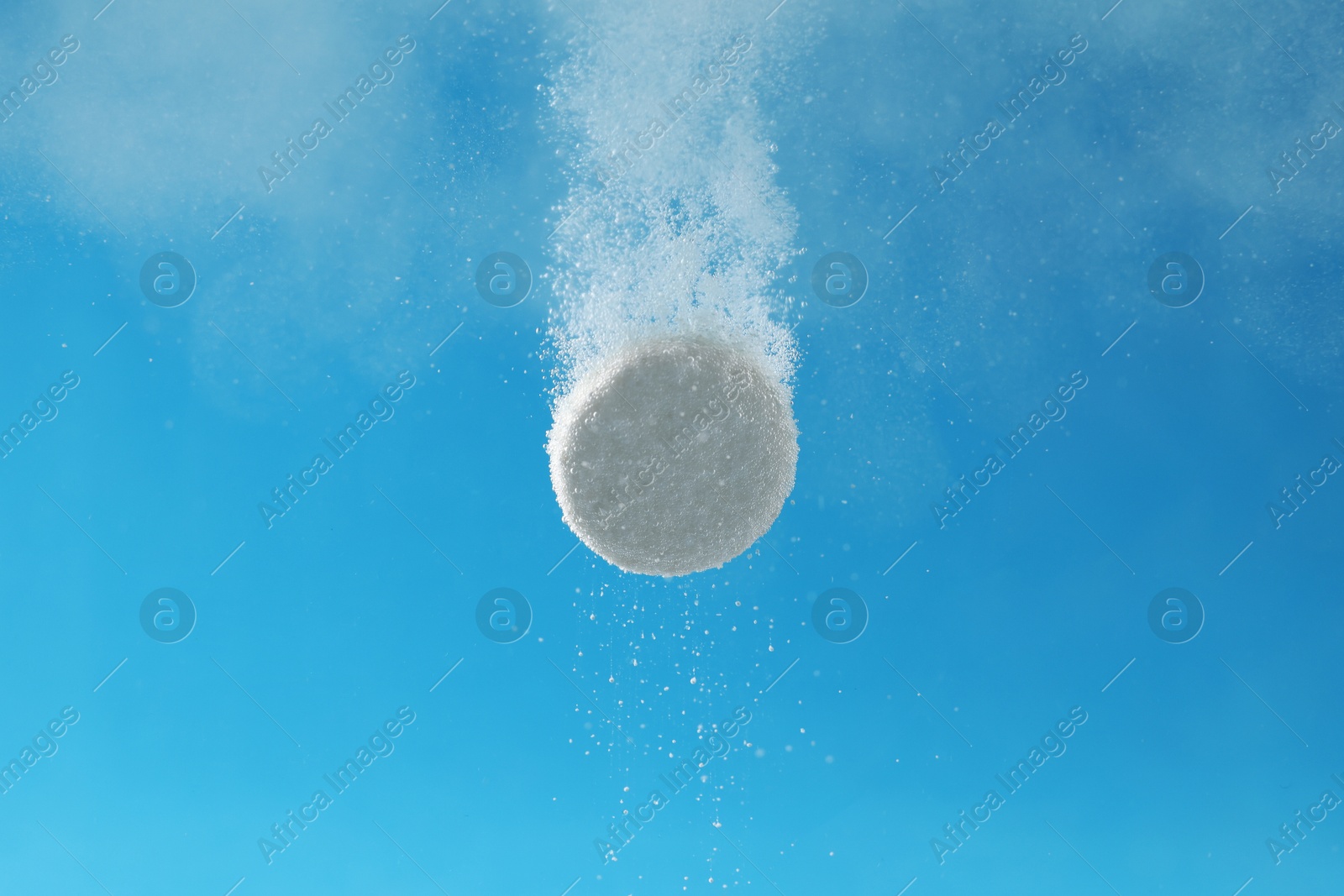 Photo of Effervescent pill dissolving in water on light blue background, closeup