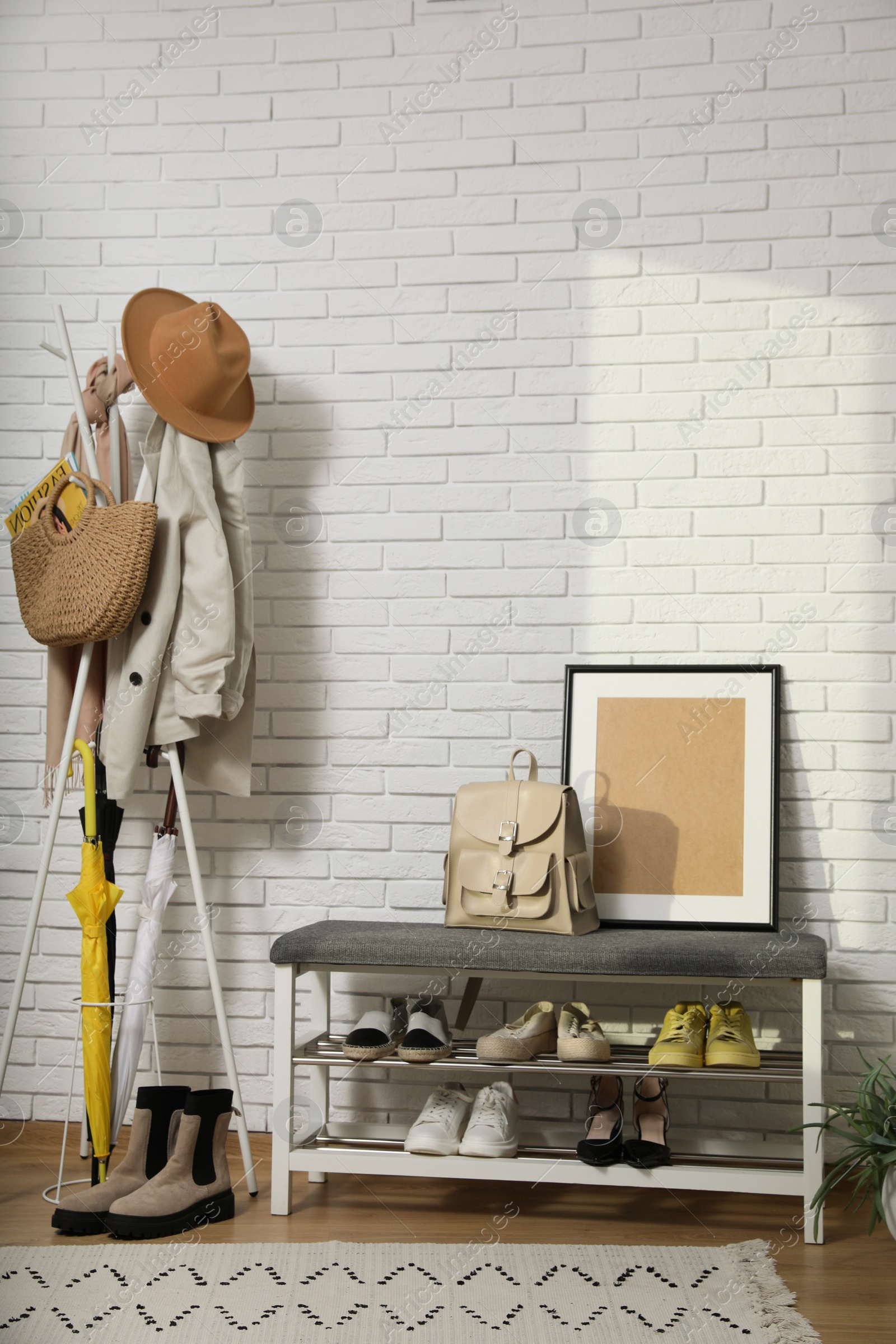 Photo of Stylish hallway interior with coat rack and shoe storage bench near white brick wall