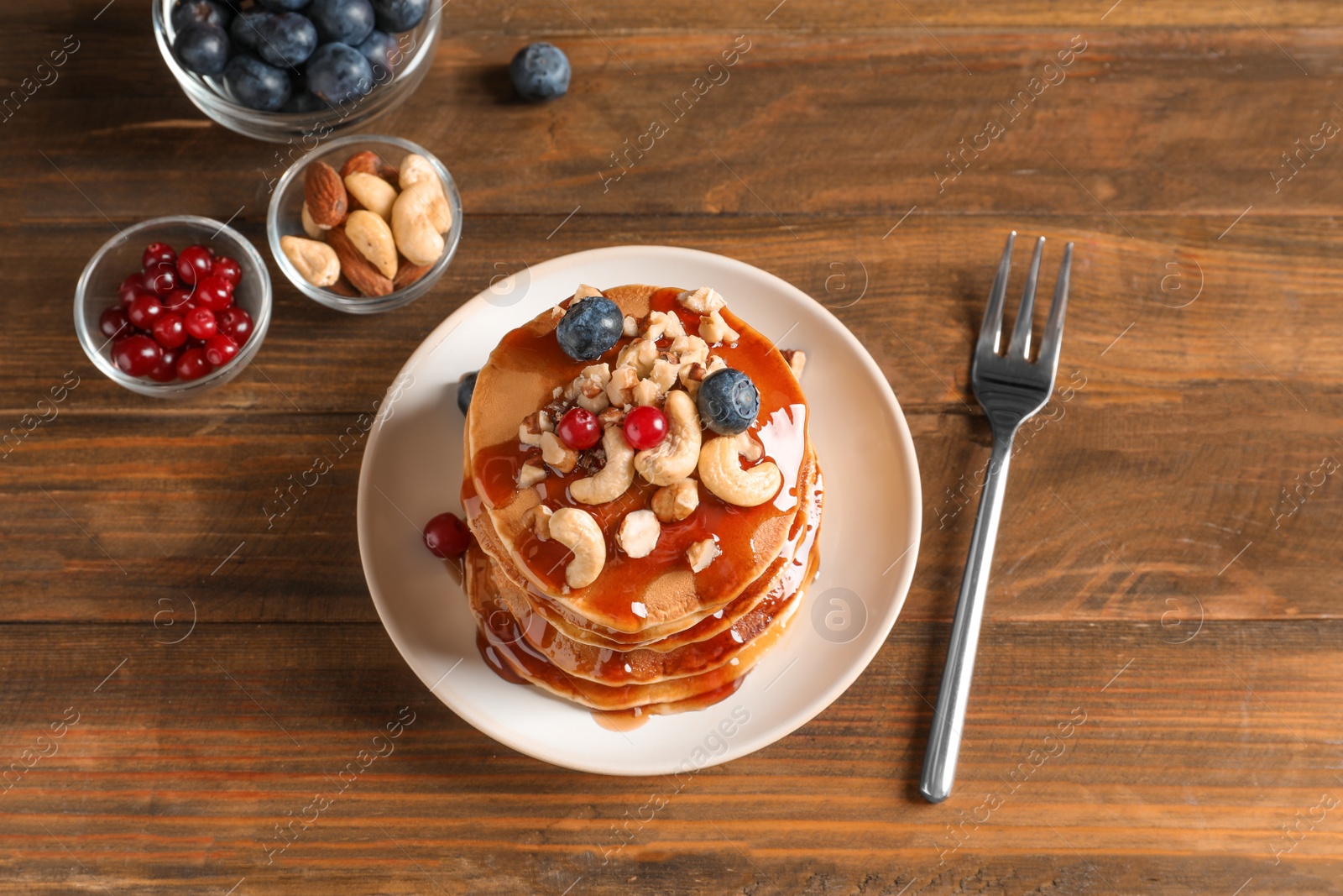 Photo of Stack of tasty pancakes with berries, nuts and syrup on table, top view