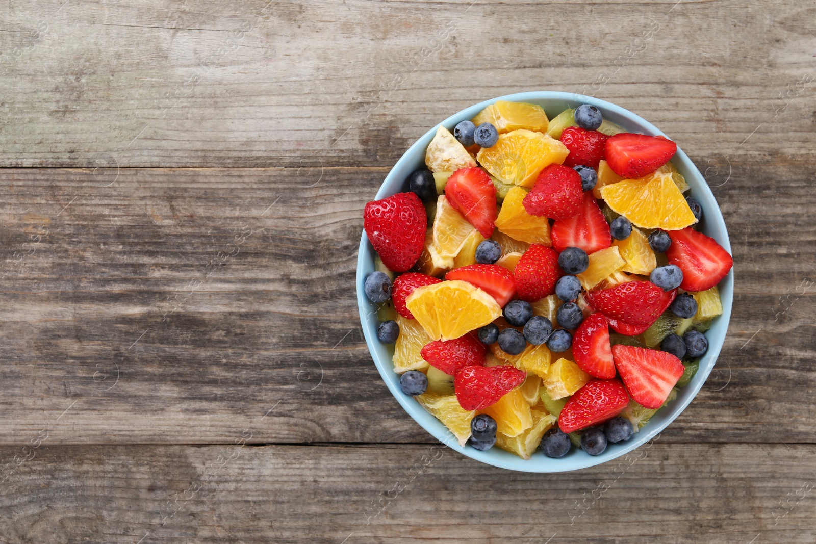 Photo of Delicious fresh fruit salad in bowl on wooden table, top view. Space for text