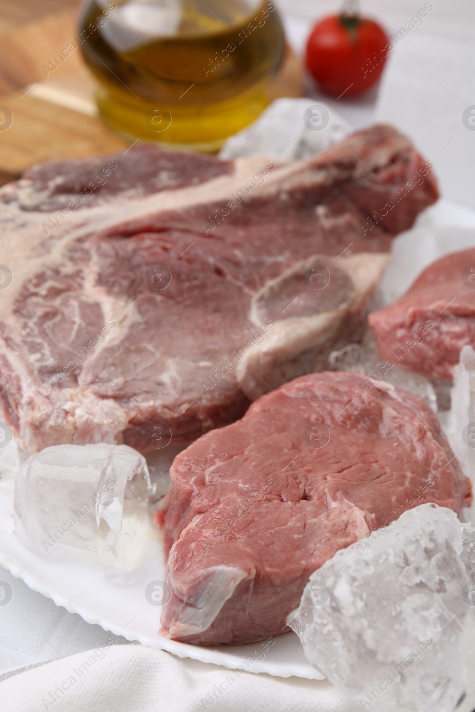 Photo of Fresh raw cut beef and ice cubes on white table, closeup