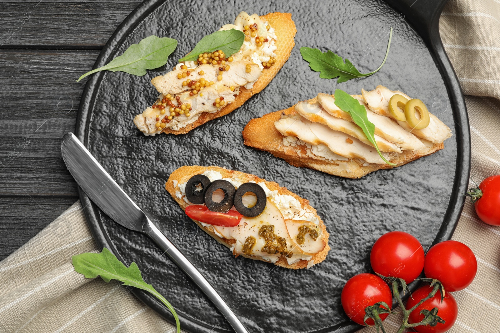 Photo of Slate plate of delicious chicken bruschettas on dark wooden table, flat lay