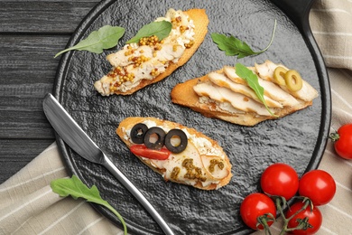 Slate plate of delicious chicken bruschettas on dark wooden table, flat lay