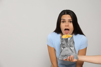 Photo of Beautiful young woman with tasty potato chips on grey background, space for text