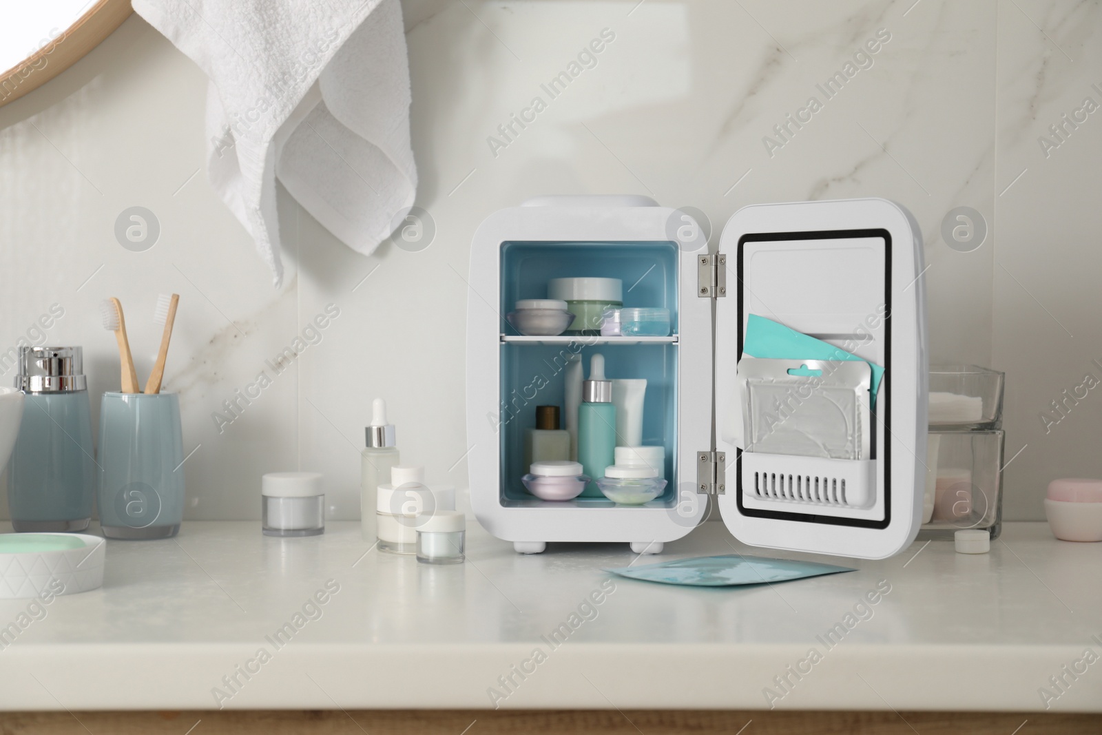 Photo of Cosmetics refrigerator and skin care products on white table indoors