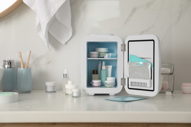 Photo of Cosmetics refrigerator and skin care products on white table indoors