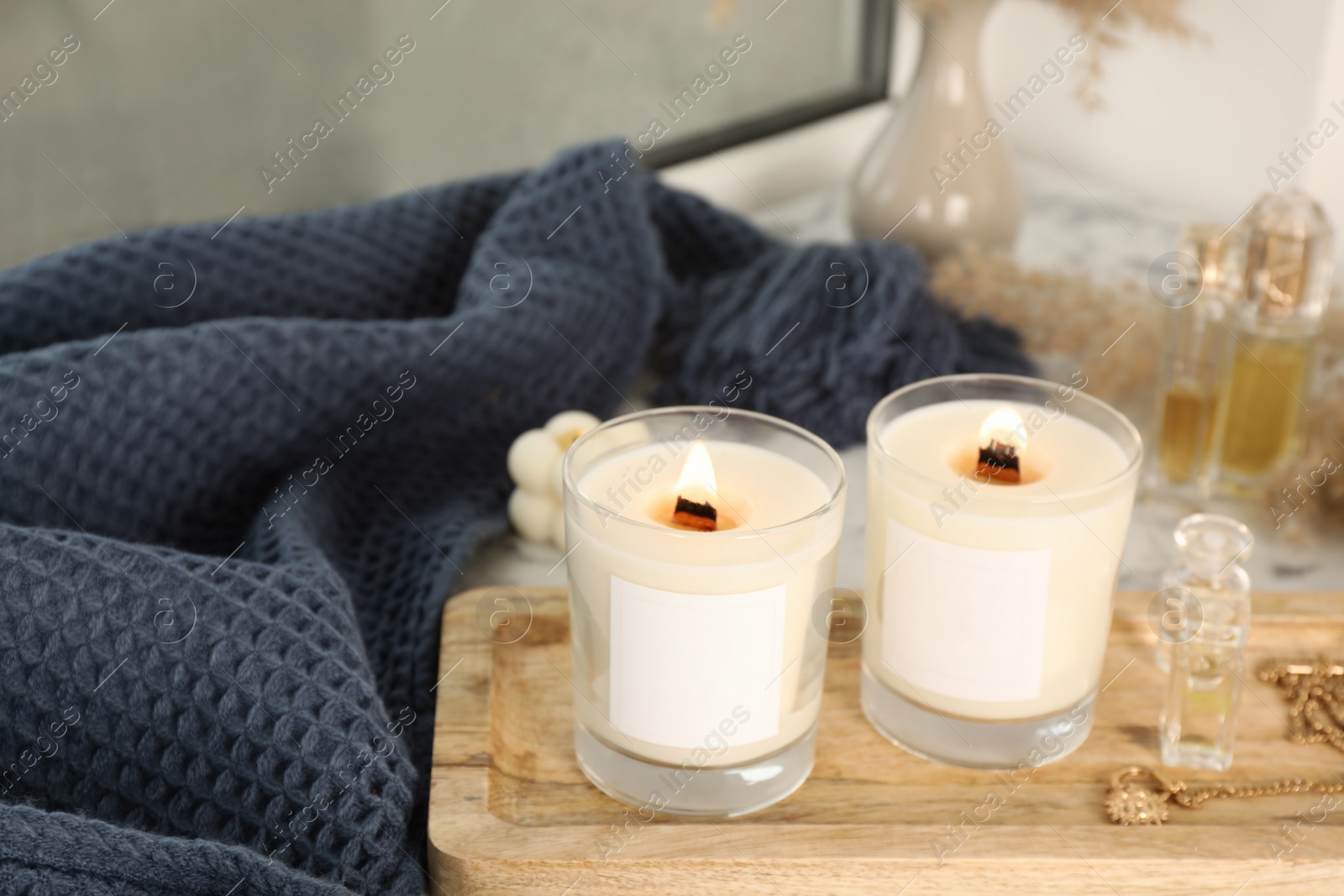 Photo of Burning soy candles, perfumes, blanket and stylish accessories on white window sill indoors