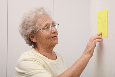 Photo of Senior woman looking at reminder note indoors. Age-related memory impairment