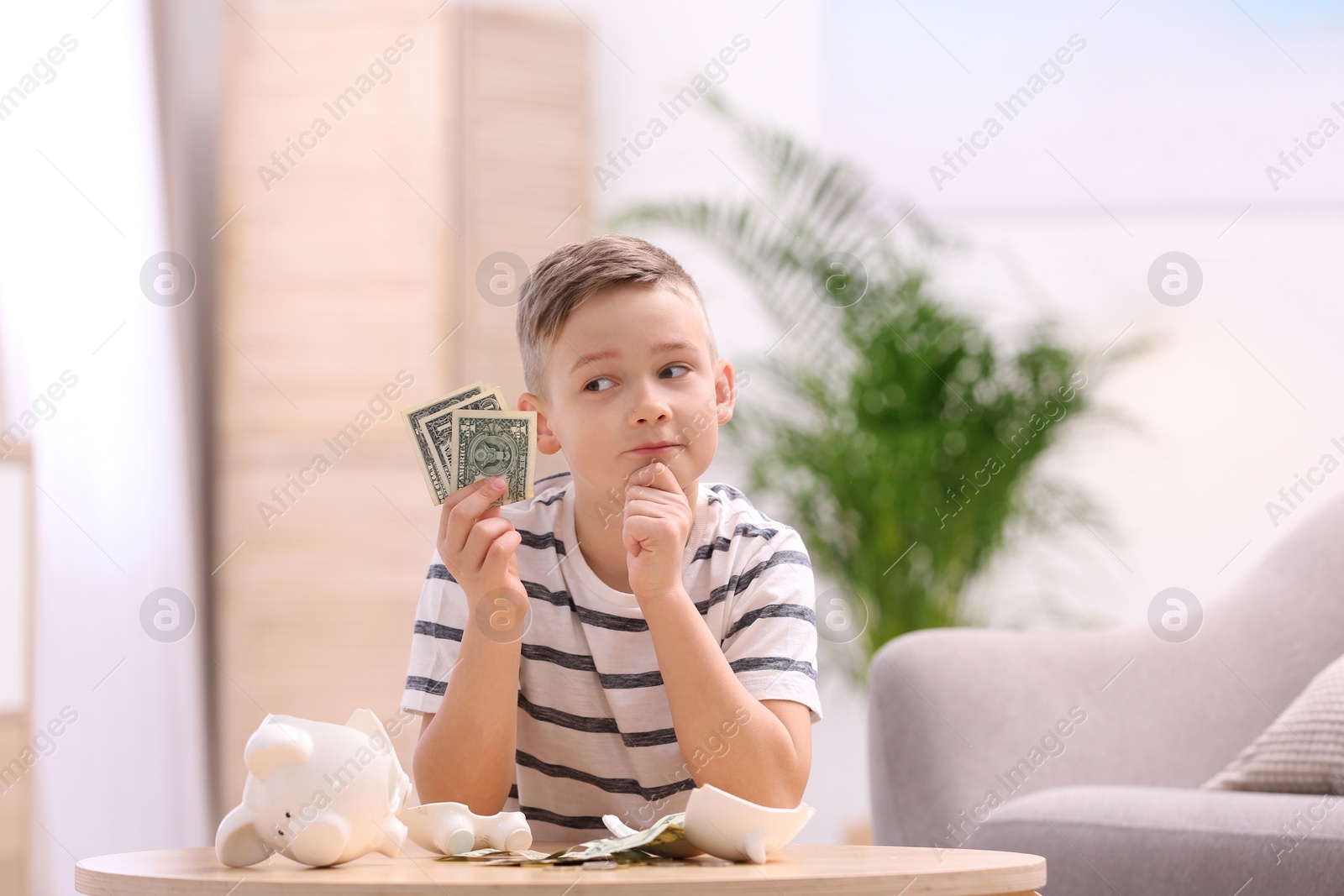 Photo of Little boy with broken piggy bank and money at home