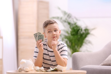 Photo of Little boy with broken piggy bank and money at home