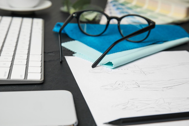 Photo of Sketches of clothes, smartphone and keyboard on black stone table, closeup. Designer's workplace