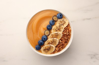 Photo of Delicious smoothie bowl with fresh blueberries, banana and granola on white marble table, top view